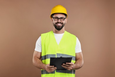 Engineer in hard hat holding clipboard on brown background