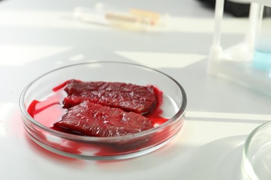 Photo of Petri dish with pieces of raw cultured meat on white table, closeup. Space for text