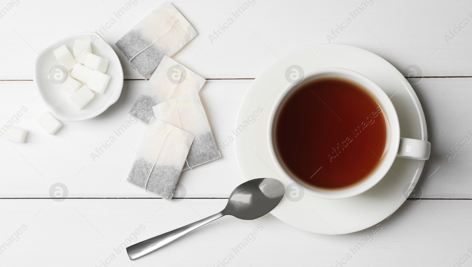 Photo of Tea bags and sugar near cup of hot drink on white wooden table, flat lay