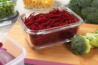 Photo of Containers with cut beetroot and fresh products on table, closeup. Food storage