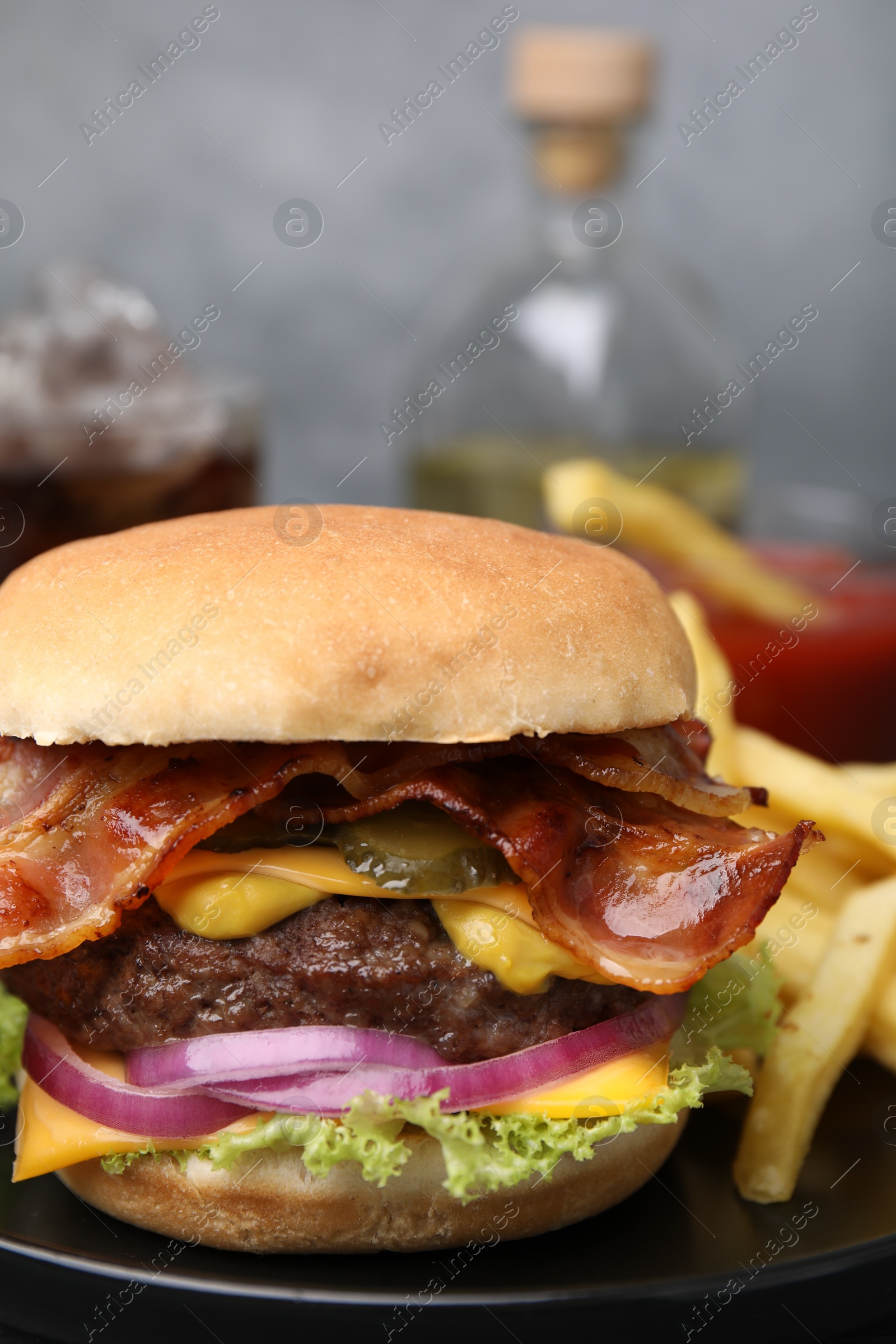 Photo of Tasty burger with bacon, vegetables and patty served with french fries on black plate, closeup