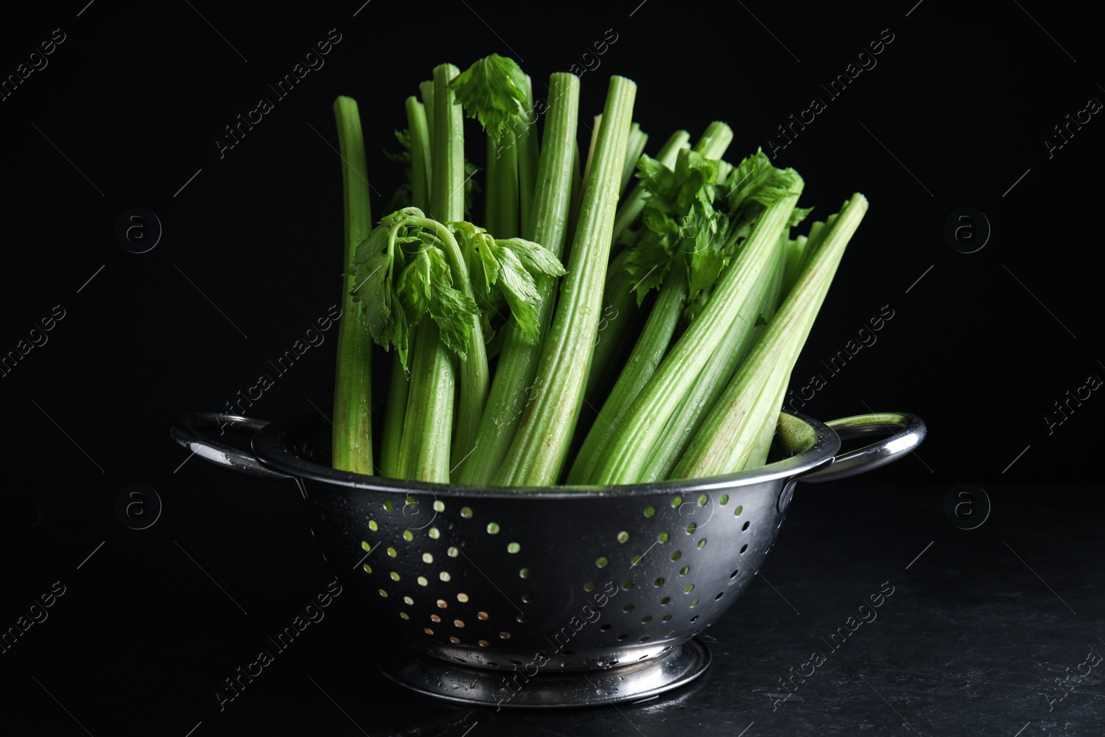 Photo of Fresh green celery in colander on black table