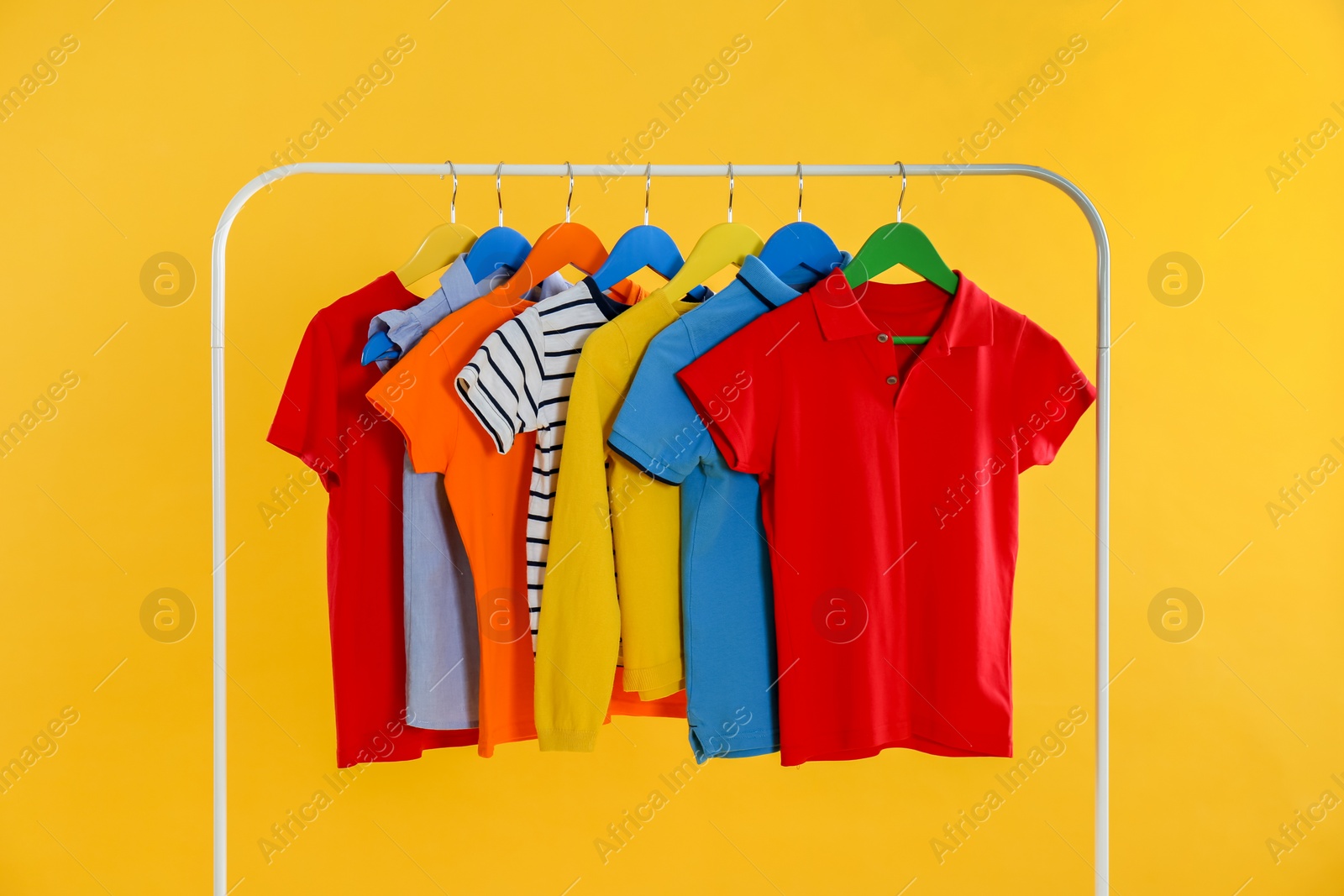 Photo of Rack with stylish children clothes on yellow background