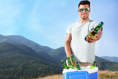 Man giving bottle from cool box in mountains. Space for text