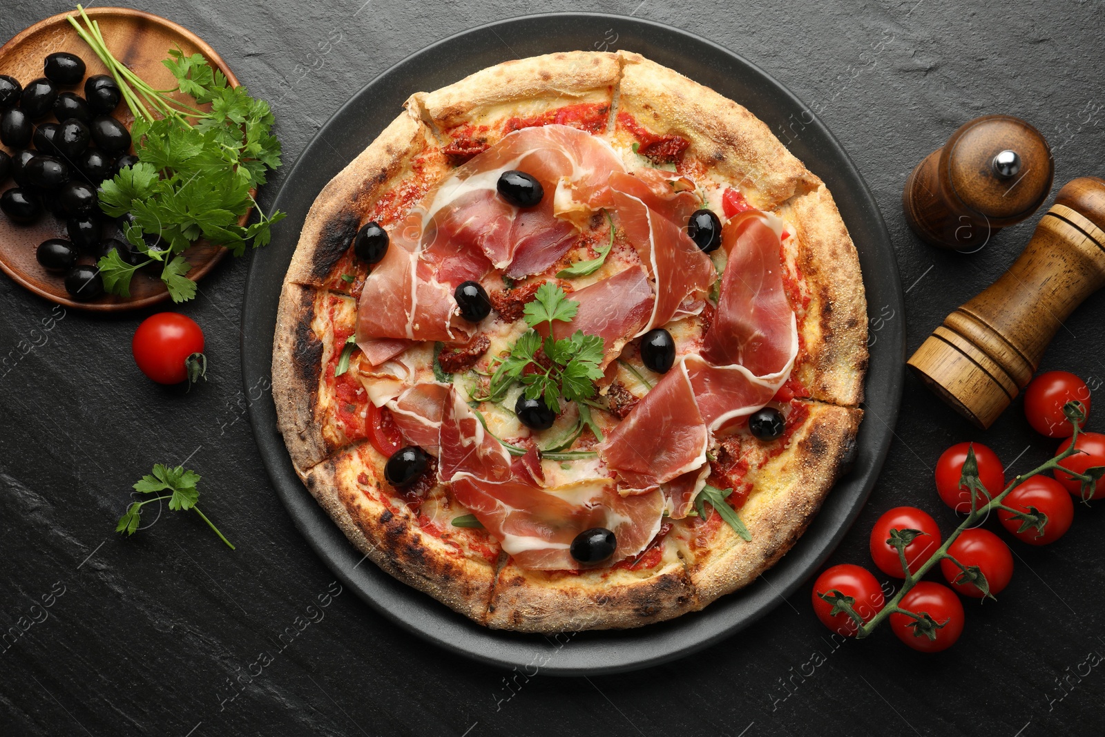 Photo of Tasty pizza with cured ham, olives, tomatoes and parsley on black table, top view