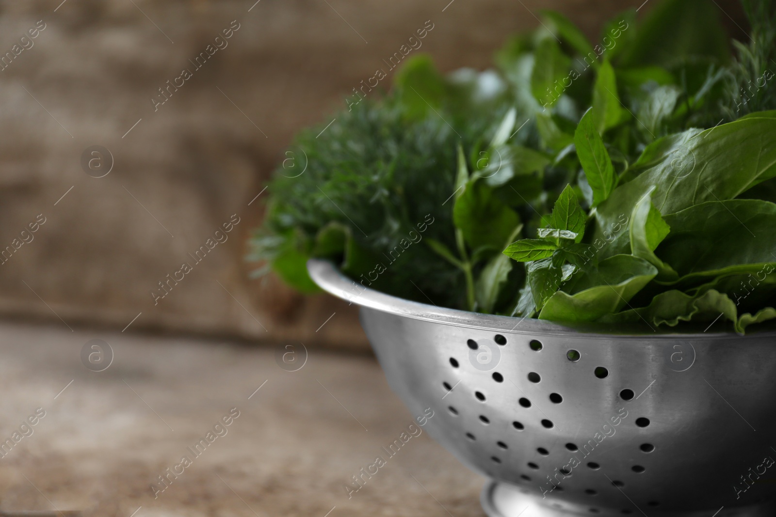 Photo of Different herbs in colander on wooden table, closeup. Space for text