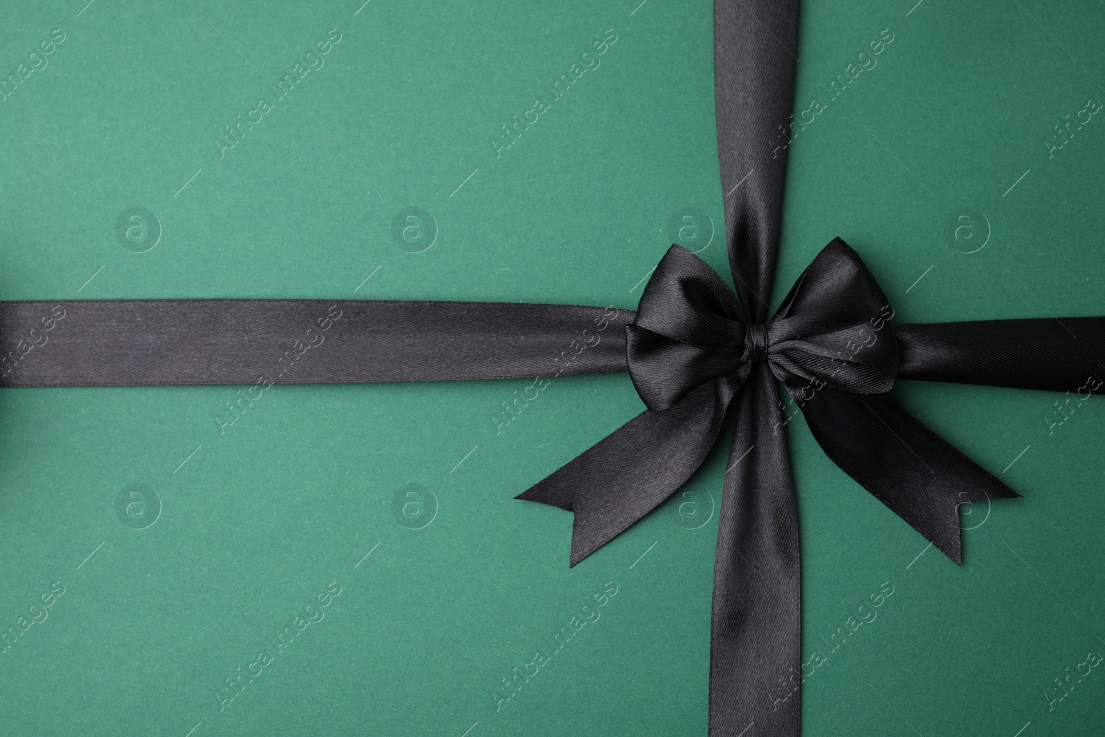 Photo of Black satin ribbon with bow on green background, top view