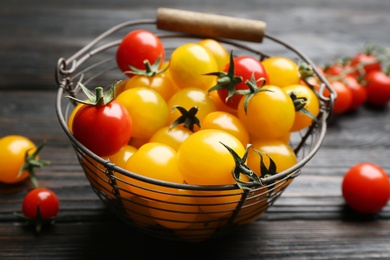 Ripe red and yellow tomatoes in metal basket on dark wooden table, closeup