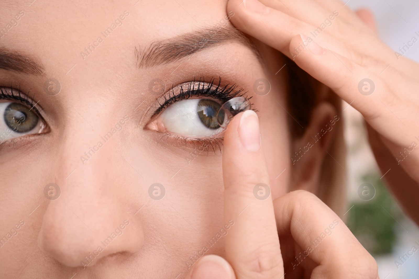 Photo of Young woman putting contact lens in her eye, closeup