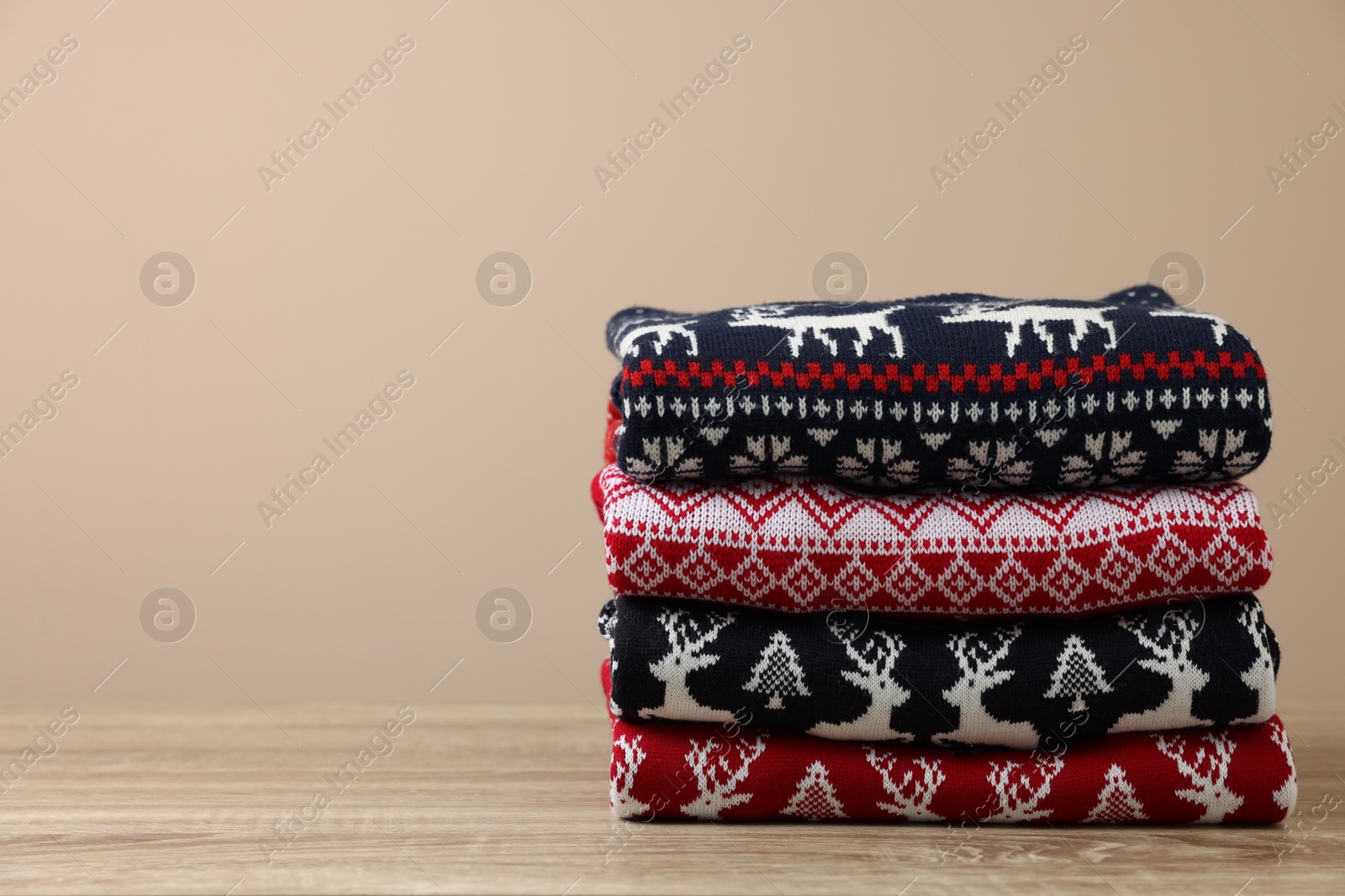 Photo of Stack of different Christmas sweaters on wooden table against beige background, space for text