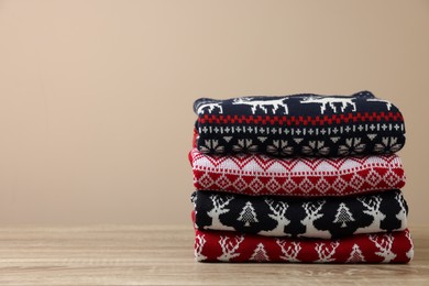 Stack of different Christmas sweaters on wooden table against beige background, space for text