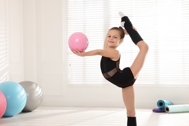 Photo of Cute little gymnast with ball doing standing split indoors