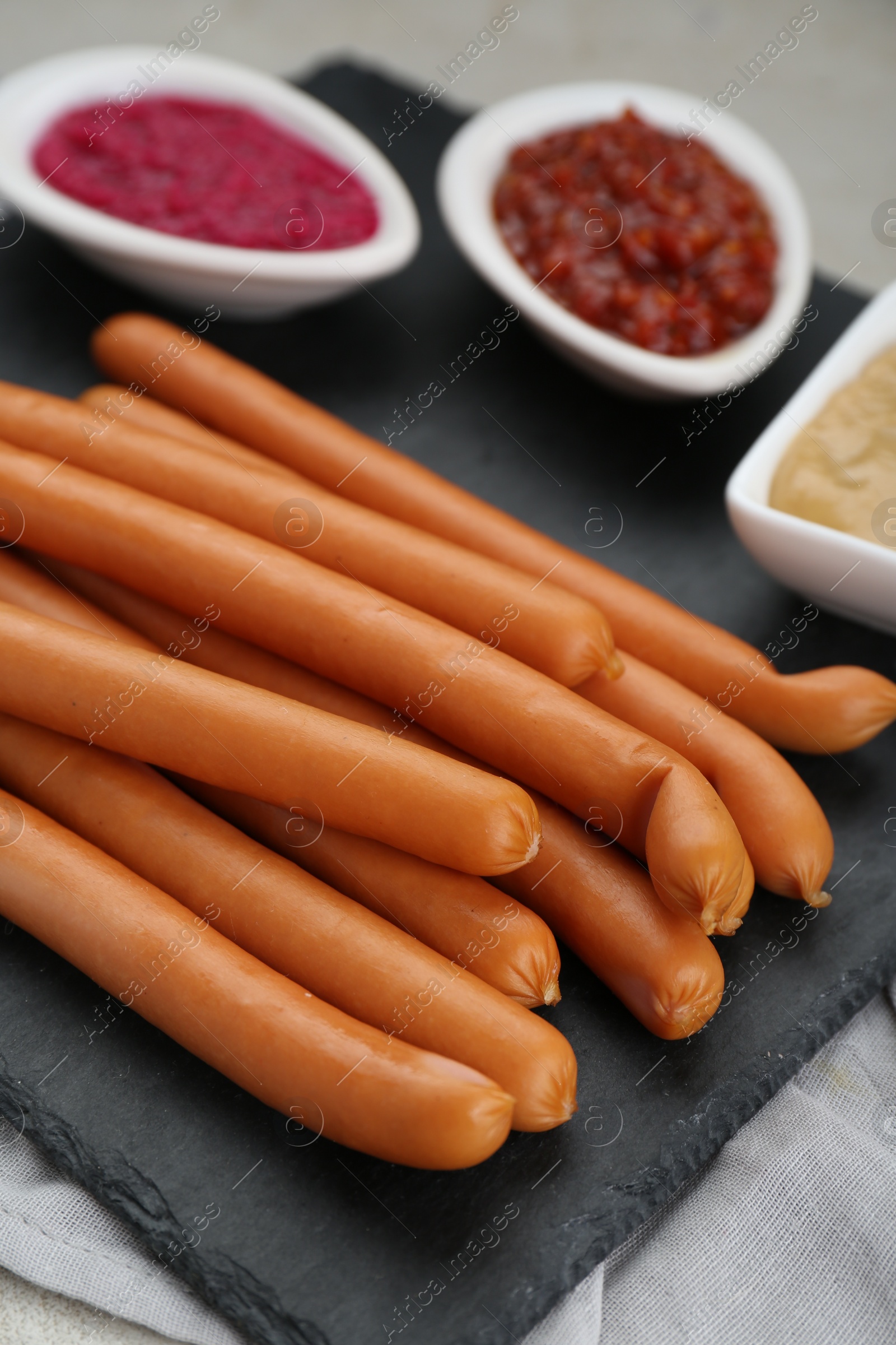 Photo of Delicious sausages, ketchup and horseradish on grey table, closeup