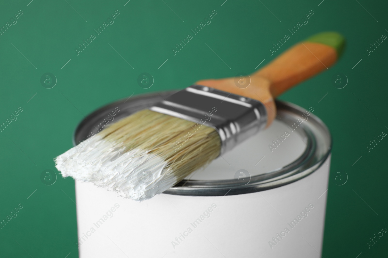Photo of Can of white paint with brush on green background