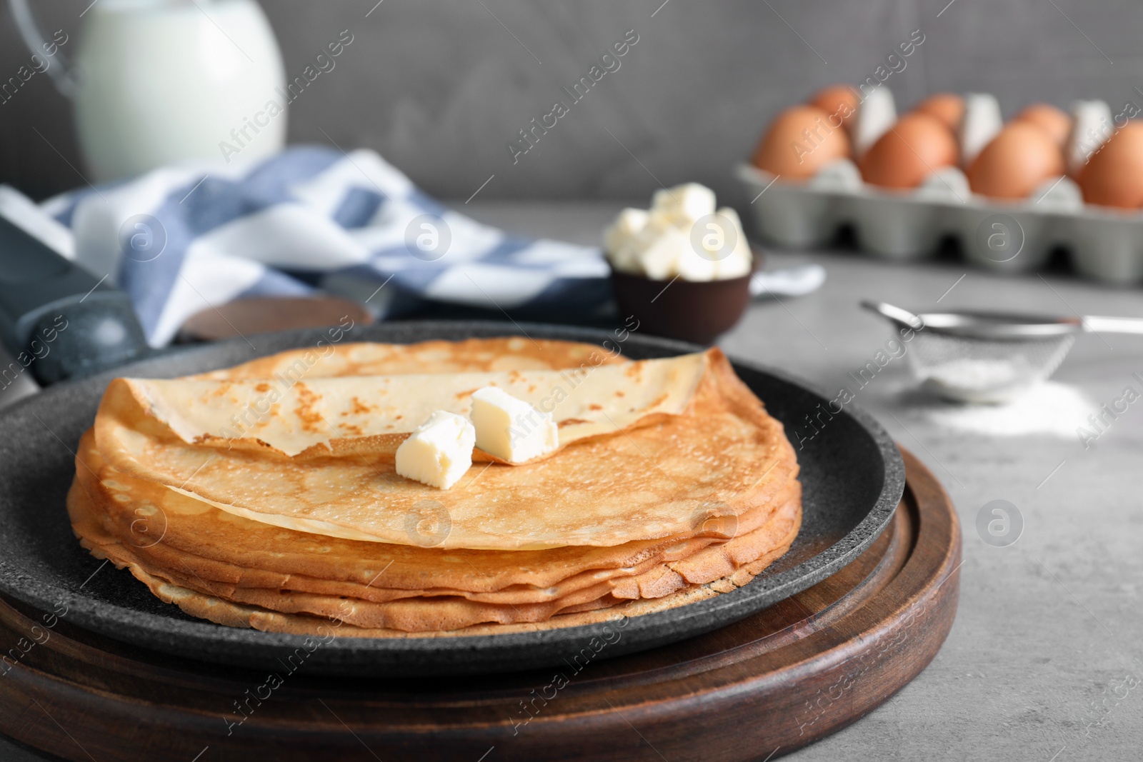 Photo of Delicious thin pancakes with butter on grey table, closeup