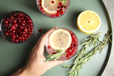 Photo of Woman holding glass of cranberry cocktail with rosemary on table, top view