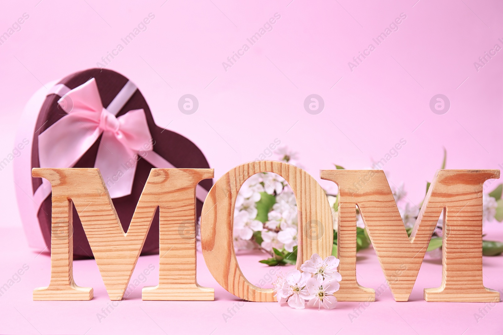 Photo of Word "MOM" made of wooden letters, flowers and gift box on table. Happy Mother's Day