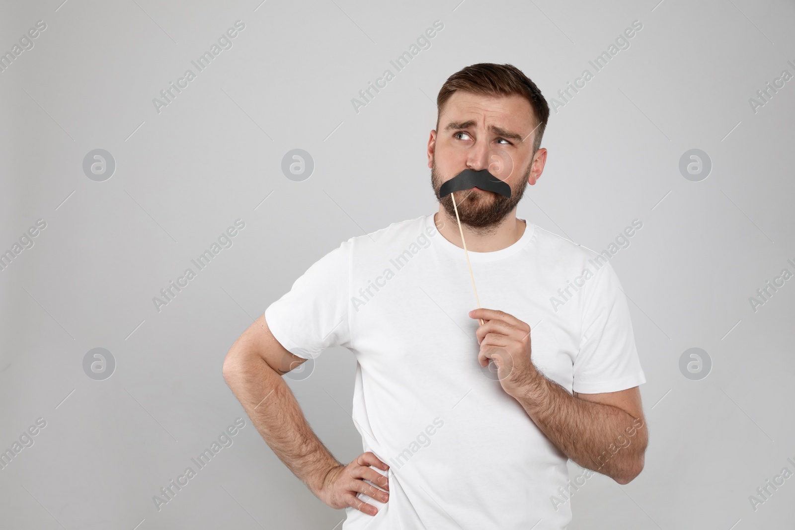 Photo of Thoughtful man with fake mustache on light grey background, space for text