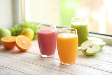 Photo of Glasses with different juices and fresh fruits on wooden window sill