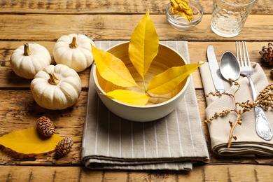 Seasonal table setting with pumpkins and autumn leaves on wooden background