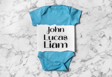 Photo of Bodysuit with different baby names on white marble background, top view
