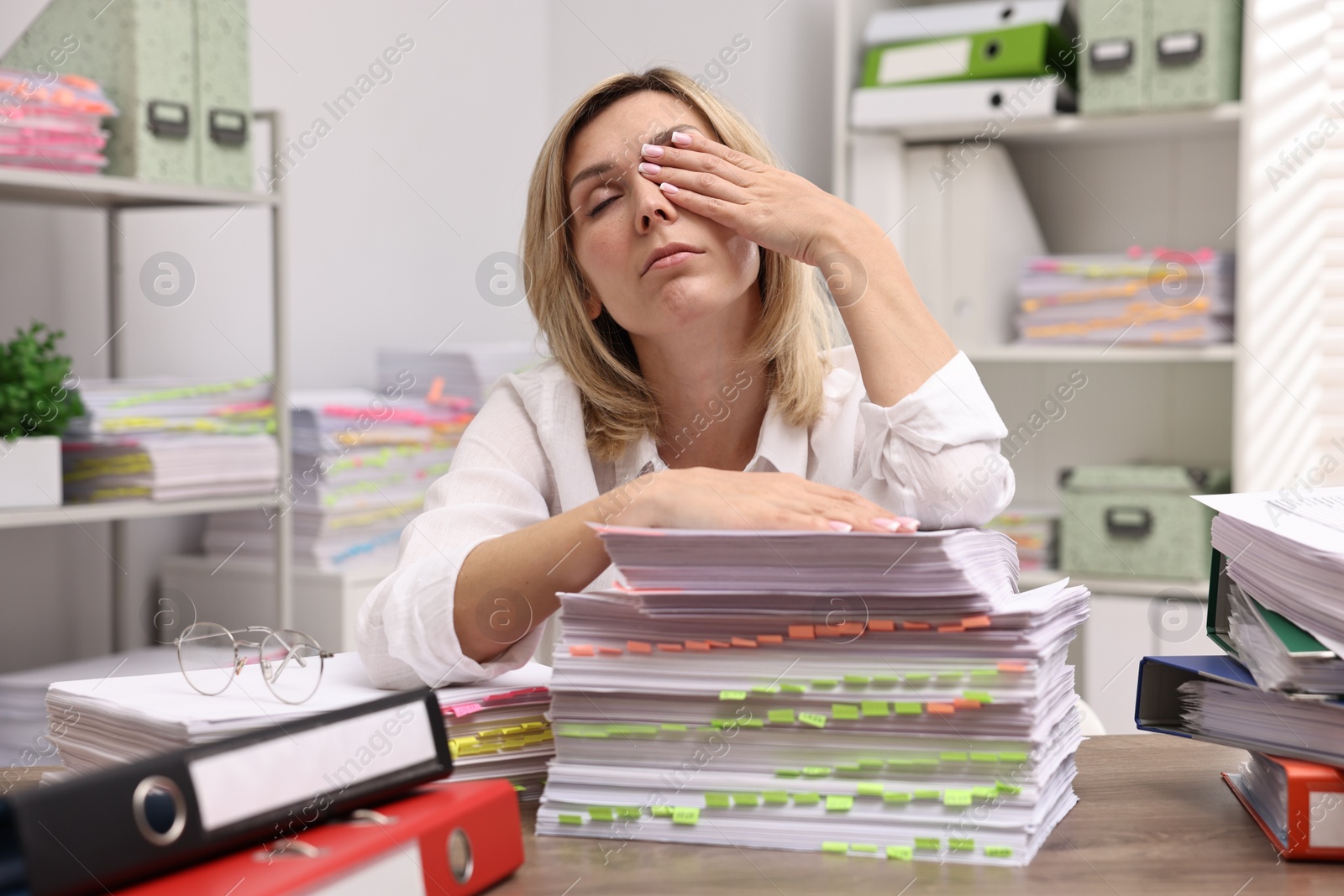 Photo of Overwhelmed woman surrounded by documents at workplace in office