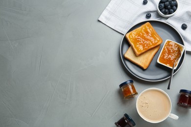 Photo of Toasts, different jams and cup of coffee served on grey table, flat lay. Space for text