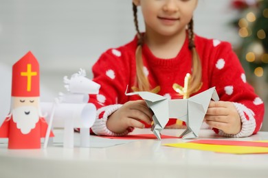 Photo of Cute little girl making paper toy for Saint Nicholas day at home, closeup