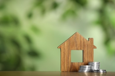 Photo of Mortgage concept. House model and coins on wooden table against blurred background, space for text
