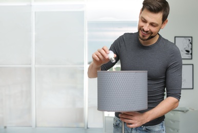 Man changing light bulb in lamp indoors