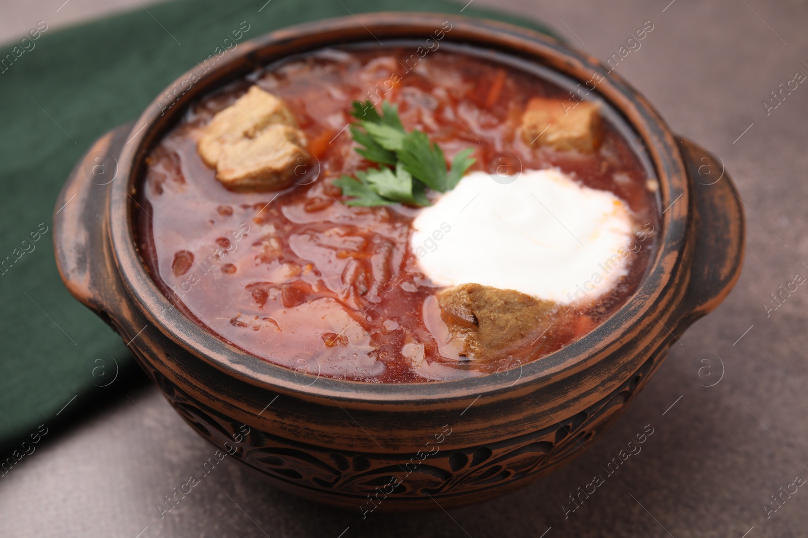 Photo of Tasty borscht with sour cream in bowl on brown textured table, closeup