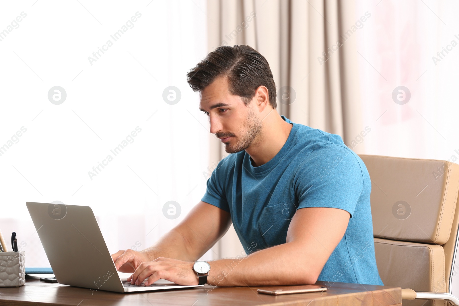 Photo of Handsome young man working with laptop at table in office