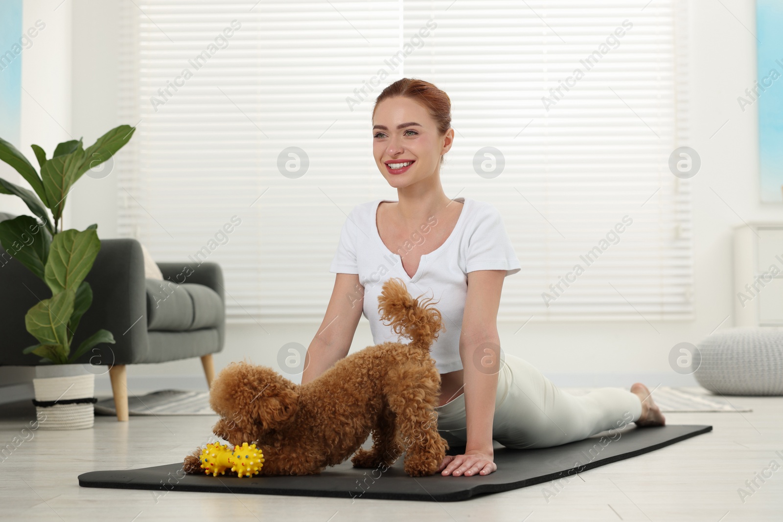 Photo of Happy young woman practicing yoga on mat with her cute dog at home