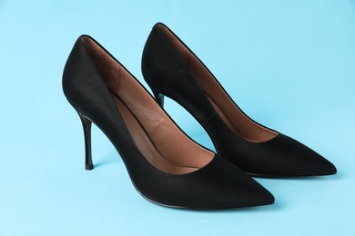 Photo of Pair of elegant black high heel shoes on light blue background