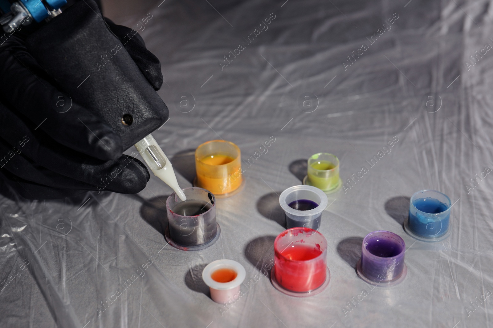 Photo of Tattoo artist dipping machine needle into ink at table, closeup