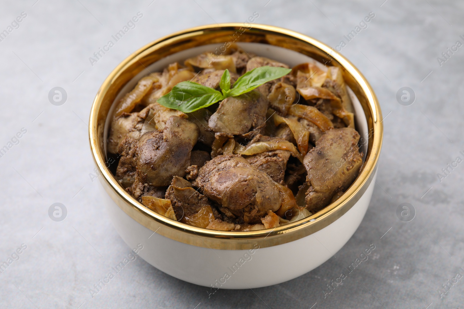 Photo of Delicious fried chicken liver with onion in bowl on light grey table, closeup