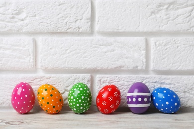 Photo of Decorated Easter eggs on table near brick wall. Space for text