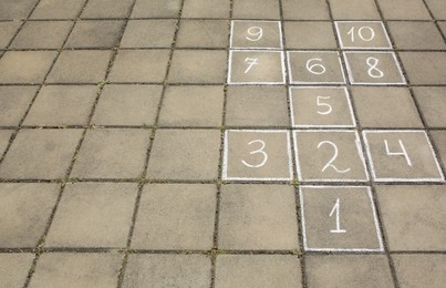 Photo of Hopscotch drawn with white chalk on street tiles outdoors. Space for text