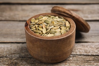 Photo of Dish with pumpkin seeds and lid on wooden table, closeup
