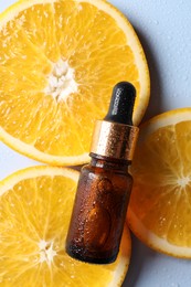 Bottle of cosmetic serum and orange slices on light blue background, flat lay