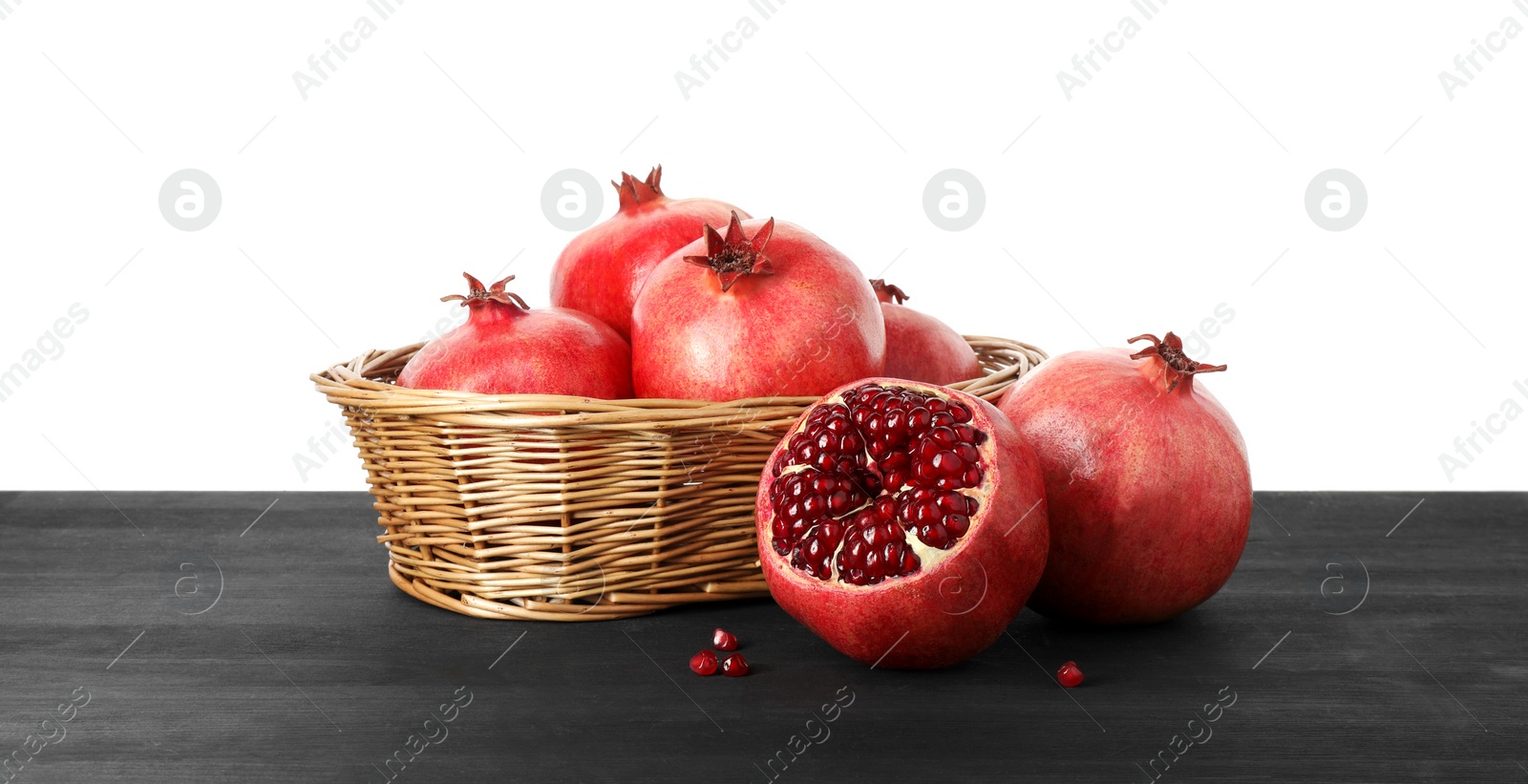 Photo of Fresh pomegranates in wicker basket on black wooden table against white background