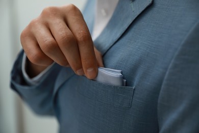 Man taking handkerchief from suit pocket on blurred background, closeup