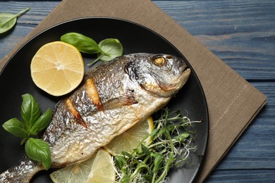 Photo of Delicious roasted fish with lemon on blue wooden table, top view