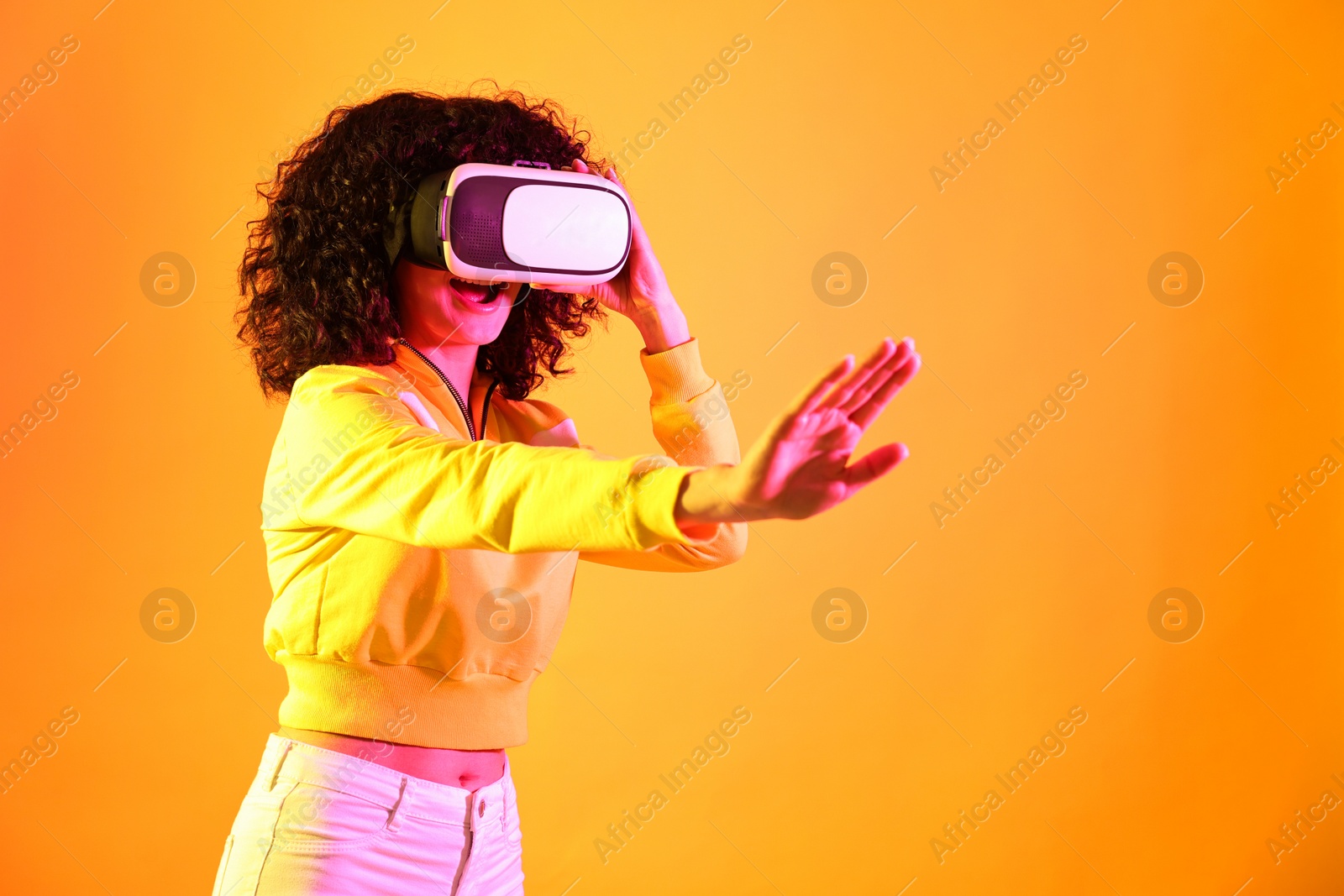 Photo of Beautiful young woman with virtual reality headset on color background in neon lights