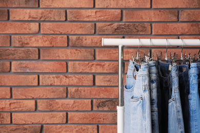 Rack with stylish jeans near brick wall. Space for text