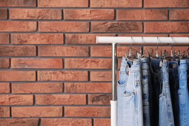 Photo of Rack with stylish jeans near brick wall. Space for text