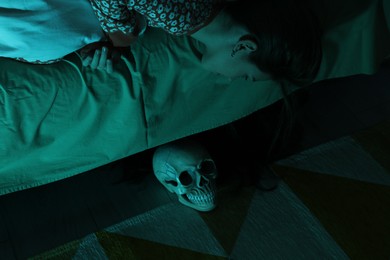 Photo of Childhood phobia. Girl looking at skull under bed indoors