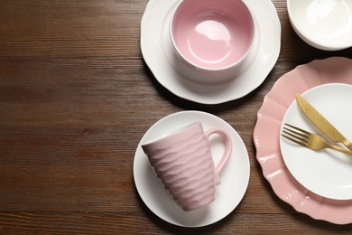 Beautiful ceramic dishware, cutlery and cup on wooden table, flat lay. Space for text