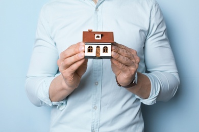 Photo of Male real estate agent with house model on light background, closeup