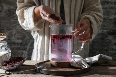 Woman putting dry hibiscus tea into teapot with boiling water at wooden table, closeup